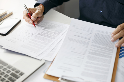 Asian businessman reviewing document reports at office workplace with computer laptop. legal expert, professional lawyer reading and checking financial documents or insurance contract