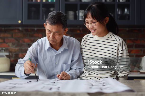 An Asian Grandfather Is Seen Teaching And Showing His Calligraphy Skills To His Granddaughter At Home The Atmosphere Is Filled With Warmth And Love As The Family Members Engage In This Traditional Chinese Activity Together Stock Photo - Download Image Now