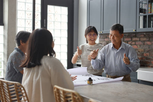 an asian grandfather is seen teaching and showing his calligraphy skills to his wife and two granddaughters at home. the atmosphere is filled with warmth and love as the family members engage in this traditional chinese activity together. - chinese script text calligraphy grandmother imagens e fotografias de stock