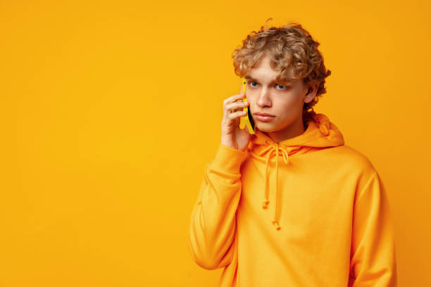 istock Young curly man speaking on mobile phone against yellow background in studio 1490868090