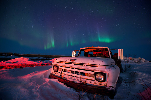 An old pick up truck stuck in the snow with the Aurora Borealis lighting up the sky above it.