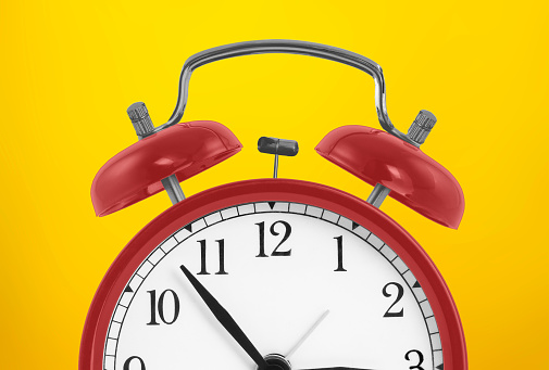 Red vintage alarm clock on bright yellow background. Minimal creative concept background