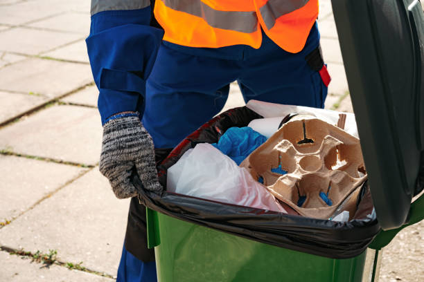 Male janitor in uniform cleans a trash can in the street stock photo