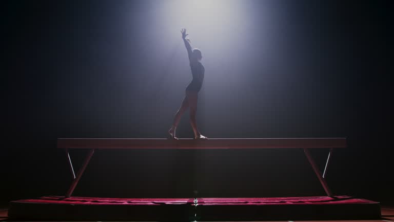 SLO MO LD Female gymnast doing a turn on the balance beam at night