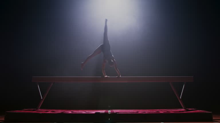 SLO MO LD Female gymnast doing a cartwheel on the balance beam at night