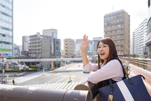 Business woman looking at view on pedestrian bridge in city - waving hand