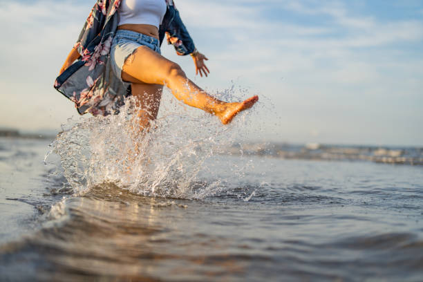 Man is standing on a sunny beach with the ocean foam washing around his feet