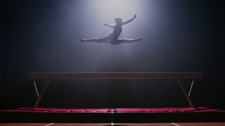 SLO MO LD Female gymnast jumping into the air on the balance beam at night