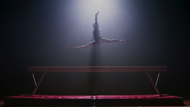 SLO MO LD Female gymnast jumping on the balance beam at night