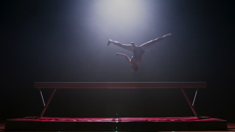 SLO MO LD Female gymnast doing a flip on the balance beam at night