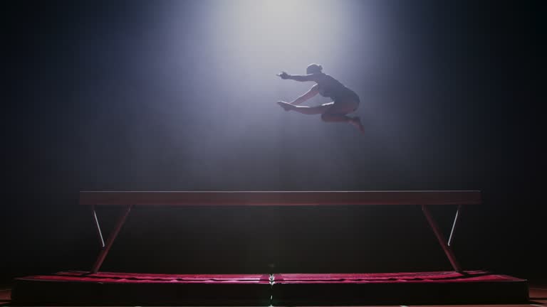 SLO MO LD Female gymnast doing a jump on the balance beam at night