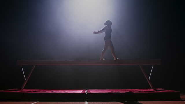 SLO MO LD Female gymnast walking on the balance beam at night and jumping off