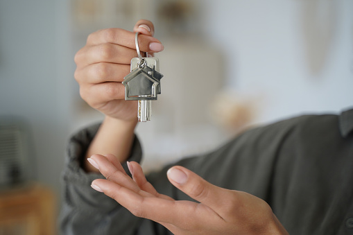Close-up of female real estate agent real estate agent tenant or homeowner showing house keys of own new home apartment, woman renter holding key bunch of housing. Rental property or mortgage concept.