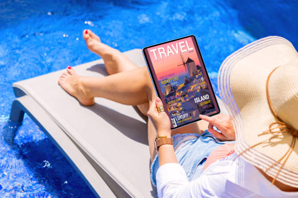 Woman reading travel magazine on tablet computer by the pool stock photo