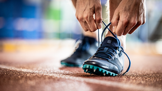 Sportsman tying sneakers shoelace while training at stadium running track close up