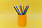 A glass with colored pencils for drawing is depicted on a yellow background. The pencils are sharpened. A great set for drawing.