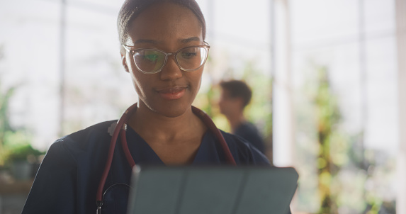 African Healthcare Nurse Using Tablet Computer for Day-to-Day Hospital Operations. Beautiful Young Clinic Professional Doing Online Medical Work in Modern Office in Public Health Care Facility