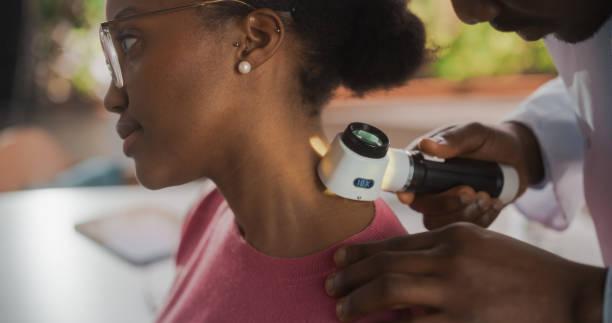 Close Up of an African Skin Care Professional Using a Dermatoscope to Examine Neck Tissue on the Skin of a Young Black Female During a Health Check Visit to a Clinic. Dermatologist in Hospital Close Up of an African Skin Care Professional Using a Dermatoscope to Examine Neck Tissue on the Skin of a Young Black Female During a Health Check Visit to a Clinic. Dermatologist in Hospital cancer screening stock pictures, royalty-free photos & images