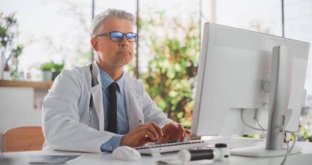 Healthcare Doctor Using Desktop Computer for Day-to-Day Hospital Operations. Clinic Professional Using PC for Efficient Online Medical Work in Modern Office in Public Health Care Facility médico de la salud que usa una computadora de escritorio para las operaciones diarias del hospital. profesional de la clínica que usa pc para un trabajo médico en línea eficiente en una oficina moderna en un centro de atención médica pública