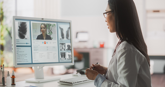 Hospital Medical Doctor Office: Portrait of Professional Female Physician Working on Desktop Computer, Talking to a Patient on a Internet Video Call Consultations, Writing Digital Prescriptions