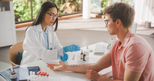 young asian allergist führt einen prick-kratztest durch, um allergische reaktionen auf den unterarm eines jungen mannes während eines gesundheitscheckbesuchs in einer medizinischen klinik zu diagnostizieren. ärztin arbeitet im krankenhaus - allergologe stock-fotos und bilder