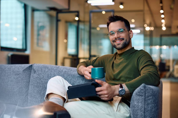 istock Happy businessman using touchpad while having cup of coffee at work and looking at camera. 1490901204