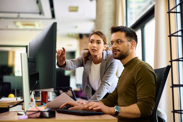 Young colleagues cooperating while working on a computer in the office. Young entrepreneur and his female coworker using desktop PC while working in the office. desktop pc stock pictures, royalty-free photos & images
