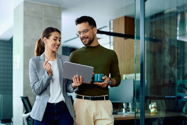 Happy colleagues using digital tablet while working in the office. Happy businesswoman and her male coworker using touchpad in the office. business people stock pictures, royalty-free photos & images
