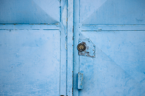 Detail of an old closed metal gate painted blue. Abstract and symmetrical image of door.
