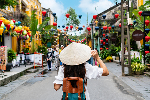 Carefree Asian tourist woman wearing Non La (traditional Vietnamese hat) enjoy sightseeing in Hoi An old town Vietnam. Copy space, closeup
