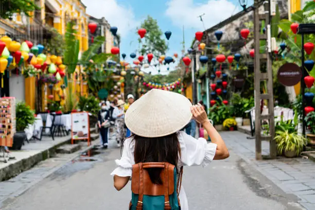 Photo of Carefree Asian tourist woman wearing Non La (traditional Vietnamese hat) enjoy sightseeing in Hoi An old town Vietnam. Copy space, closeup
