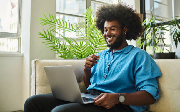 istock Happy, young black man with an afro, sitting on the couch whilst looking at his laptop computer screen. 1490903402