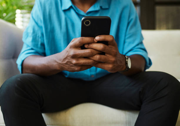 istock Unrecognised man wearing a blue shirt sitting on a sofa whilst texting on his mobile phone. Stock photo 1490903526