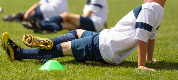 jeune garçon roulant le veau à l’aide d’un rouleau en mousse au terrain d’entraînement. unité d’entraînement de soccer scolaire pour jeunes athlètes - foot massage photos et images de collection