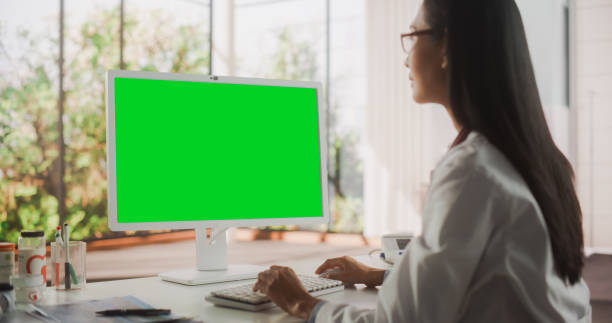 istock Young Female Doctor Wearing White Coat, Working on Personal Computer with Green Screen Mock Up Display in Her Office. Beautiful Asian Medical Health Care Professional Working with Test Results 1490905313