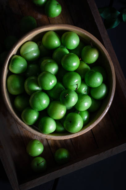Fresh green plums in bowl on wooden background.