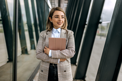 Well dressed businesswoman walking in front of big company, holding digital tablet in hands
