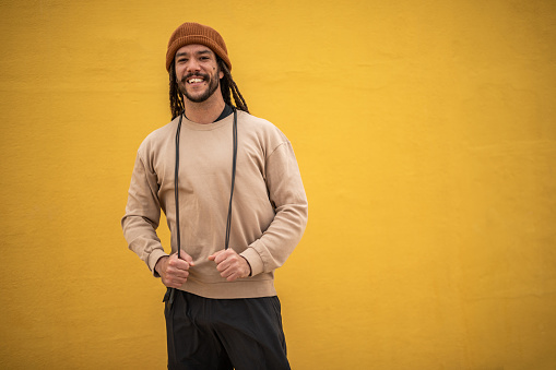 Dedication, sports discipline and daily training strengthen the spirit and body. A Spanish man with dreadlocks stands next to a yellow wall and trains with rubber resistance bands