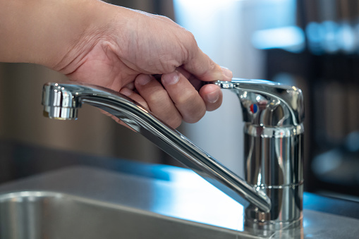 Save water or water conservation concepts. Male hand closing water tap or faucet on stainless steel sink in the kitchen.