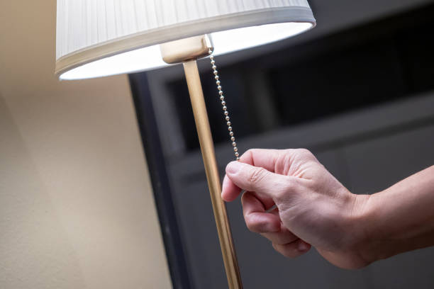 istock Saving electricity energy concept. Male hand pulling light switch chain on white lamp in the bedroom. Turn off lighting equipment for bedtime. 1490918423