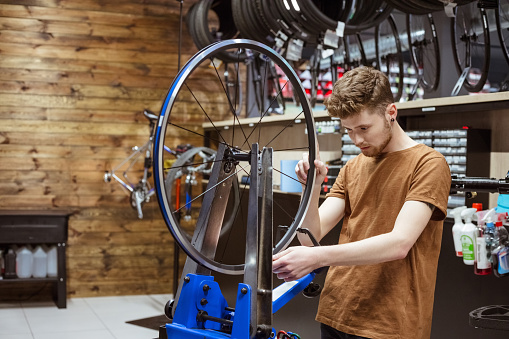 Serviceman centering the bicycle wheel in bike workshop.