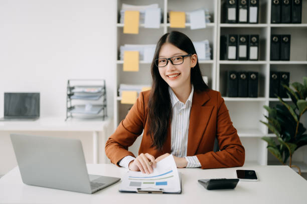 istock Confident beautiful Asian businesswoman typing laptop computer and digital tablet while holding coffee at office 1490919331