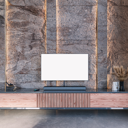 Modern living room with a  blank TV (copy space) and decoration (vases with dried plants, books, origami paper bird, remote control, gift bag) on a low dark gray and wooden paneled cabinet in front of an illuminated modern brown marble tiled wall background, on the polished modern cement floor. 3D rendered image.