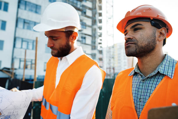 istock Two young male engineers in uniform and hardhats working at construction site 1490920359