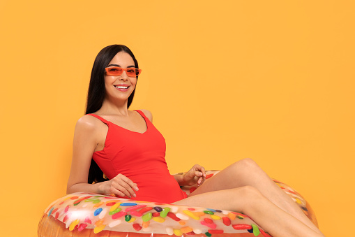 Happy young woman with beautiful suntan and sunglasses on inflatable ring against orange background