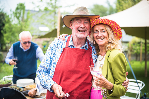 Beautiful elderly couple preparing food for barbecue and toasting with wine, outdoor picnic in the garden of the house, portrait of healthy, happy and in love senior people