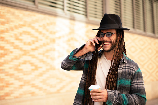 Handsome guy drinking coffee while walking in the street. Modern fashion man using the phone.