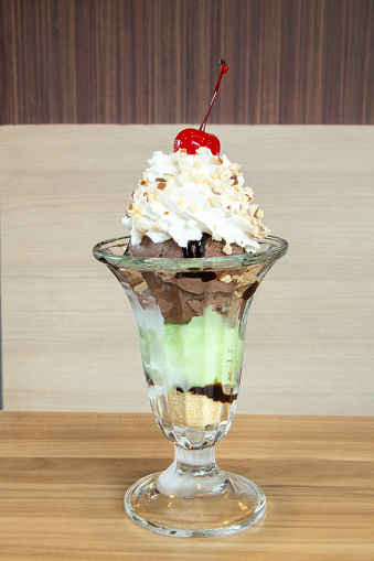 Ice cream sundae in a glass topped with whipped cream and nuts with 3 other flavors of ice cream