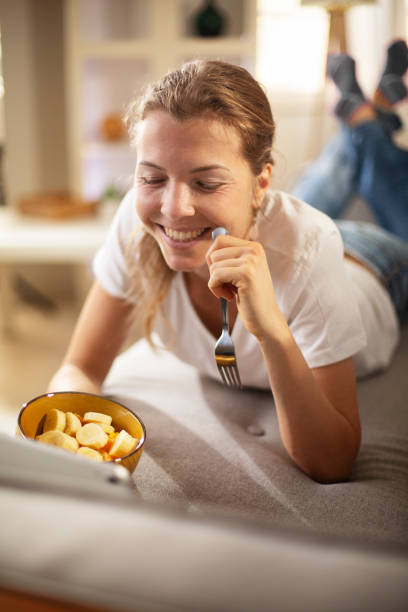 istock Beautiful woman sitting on sofa, eating fruit 1490930352
