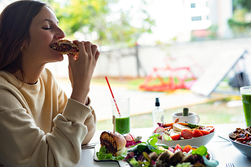 Woman wearing eyeglasses eating a hamburger. Full mouth oen biting